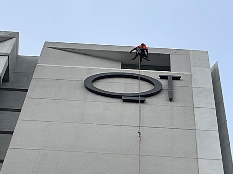 A person suspended by ropes, performing exterior cleaning on a high-rise building, wearing full safety gear, including a harness, helmet, and gloves.
