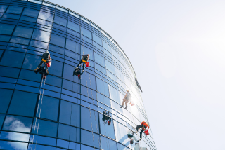 Three rope access technicians clean the glass windows of a high-rise building.
