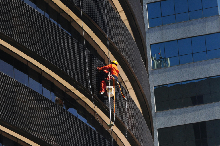 Three rope access technicians clean the glass windows of a high-rise building.