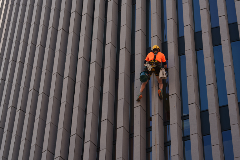 Three rope access technicians clean the glass windows of a high-rise building.
