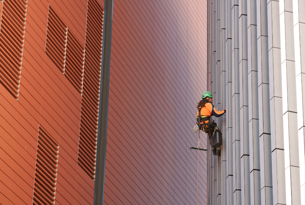 Two rope access workers suspended on the side of a high-rise building, cleaning glass windows with safety harnesses and professional equipment.